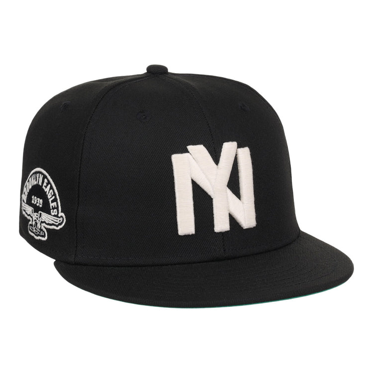 The Ebbets Field Brooklyn Eagles NLB Fitted Ballcap is a black cap with large white overlapping NY letters on the front and a patch showing an eagle and 