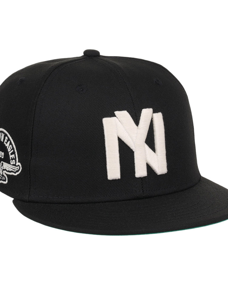 The Ebbets Field Brooklyn Eagles NLB Fitted Ballcap is a black cap with large white overlapping NY letters on the front and a patch showing an eagle and 