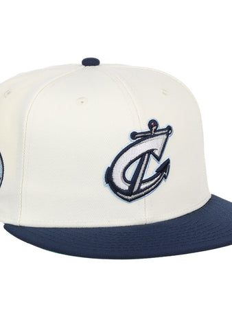 The Ebbets Field Columbus Clippers MiLB Snapback Ballcap is a white hat with a navy blue brim, featuring a stylized anchor and C logo on the front and a circular 614 cityscape patch on the side.