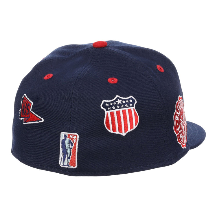 The Washington Black Senators NLB Varsity Fitted Ballcap by Ebbets Field is a navy cap featuring embroidered patches: a stars-and-stripes shield, red pennant, round red and white badge, and a small silhouette logo.