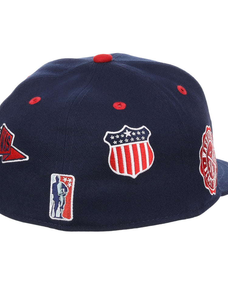 The Washington Black Senators NLB Varsity Fitted Ballcap by Ebbets Field is a navy cap featuring embroidered patches: a stars-and-stripes shield, red pennant, round red and white badge, and a small silhouette logo.