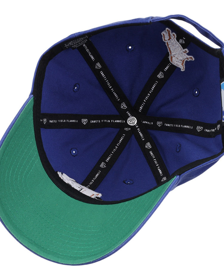 A look inside the blue Durham Bulls MiLB Dad Ballcap by Ebbets Field, featuring a green brim, black interior taping with white text and logos, metal eyelets, and an inner horse logo patch.