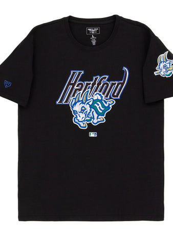 The Ebbets Field Hartford Yard Goats MiLB Fashion Cotton Short Sleeve Tee features a black design with a blue and white Hartford logo, a cartoon blue dinosaur on the chest, and a smaller dinosaur graphic on the left sleeve.