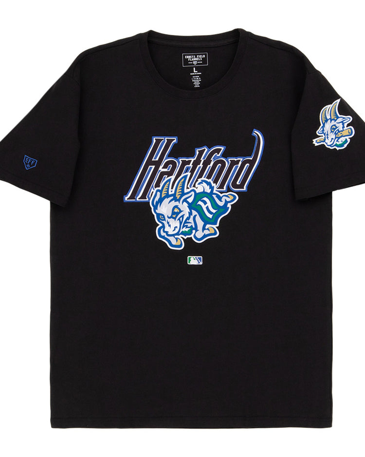 The Ebbets Field Hartford Yard Goats MiLB Fashion Cotton Short Sleeve Tee features a black design with a blue and white Hartford logo, a cartoon blue dinosaur on the chest, and a smaller dinosaur graphic on the left sleeve.