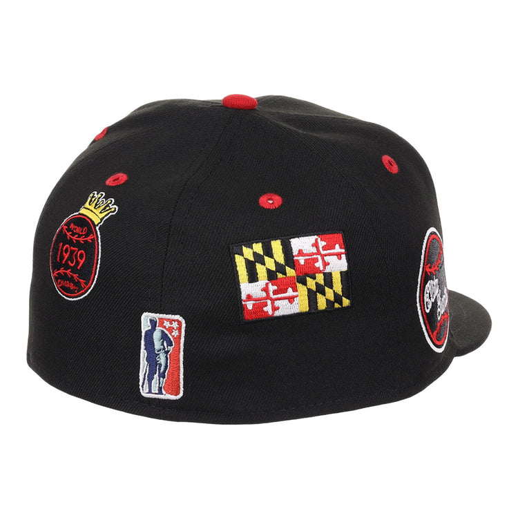 The Baltimore Elite Giants NLB Varsity Fitted Ballcap by Ebbets Field is a black cap featuring red, yellow, and white embroidered patches: a Maryland flag, a basketball-themed logo, and a person holding a basketball.