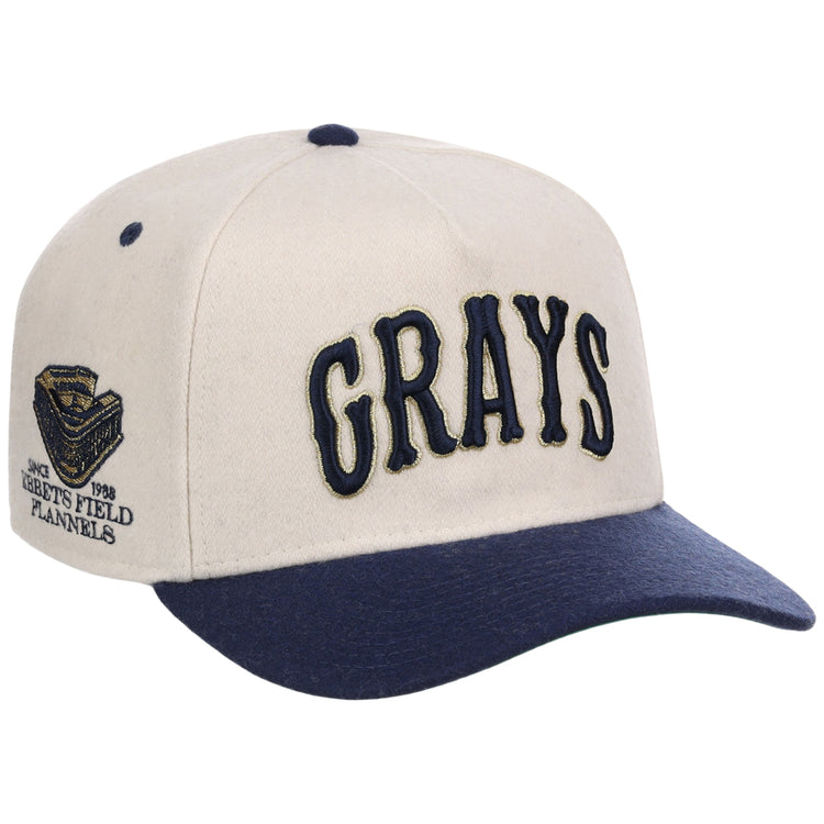 The Homestead Grays NLB Ballpark A-Frame Ballcap by Ebbets Field features a beige crown, navy brim, large navy “GRAYS” embroidery on the front, and a detailed side patch with text and a stadium graphic.
