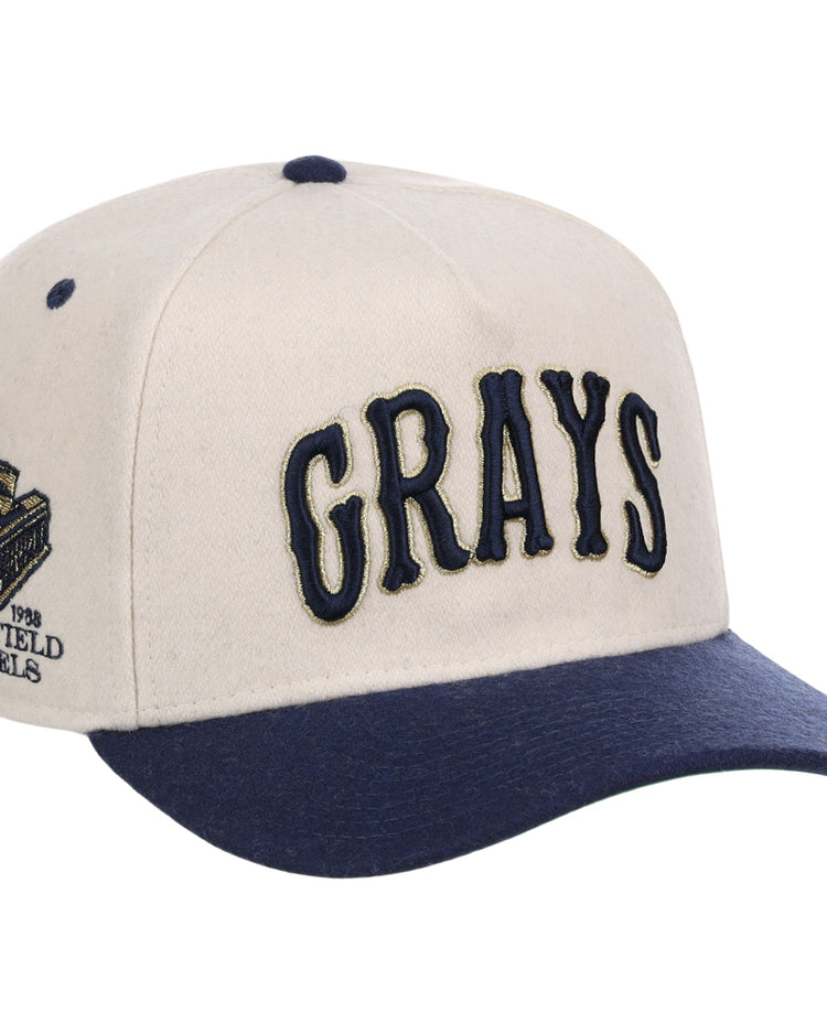 The Homestead Grays NLB Ballpark A-Frame Ballcap by Ebbets Field features a beige crown, navy brim, large navy “GRAYS” embroidery on the front, and a detailed side patch with text and a stadium graphic.