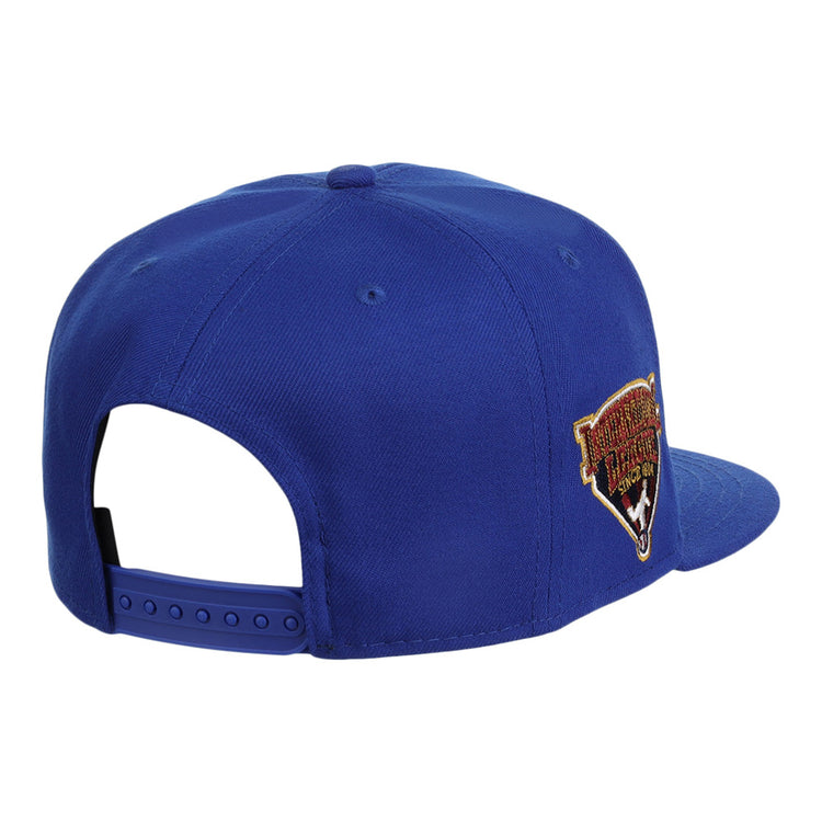 The Ebbets Field Durham Bulls MiLB Snapback Ballcap is blue, features an adjustable strap, and has a colorful embroidered patch on the side, shown from a rear and slightly angled view.