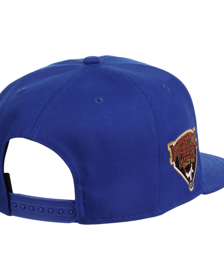 The Ebbets Field Durham Bulls MiLB Snapback Ballcap is blue, features an adjustable strap, and has a colorful embroidered patch on the side, shown from a rear and slightly angled view.