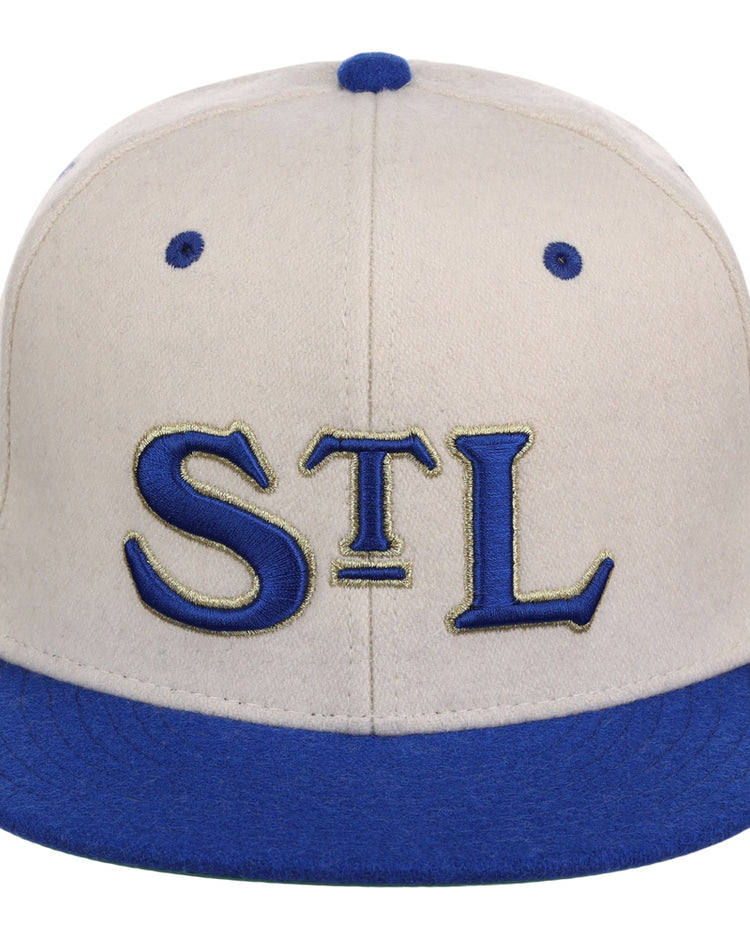 The Ebbets Field St. Louis Stars NLB Ballpark Fitted Ballcap has a beige crown, blue bill, blue accents, and features “STL” in blue and gold on the front.