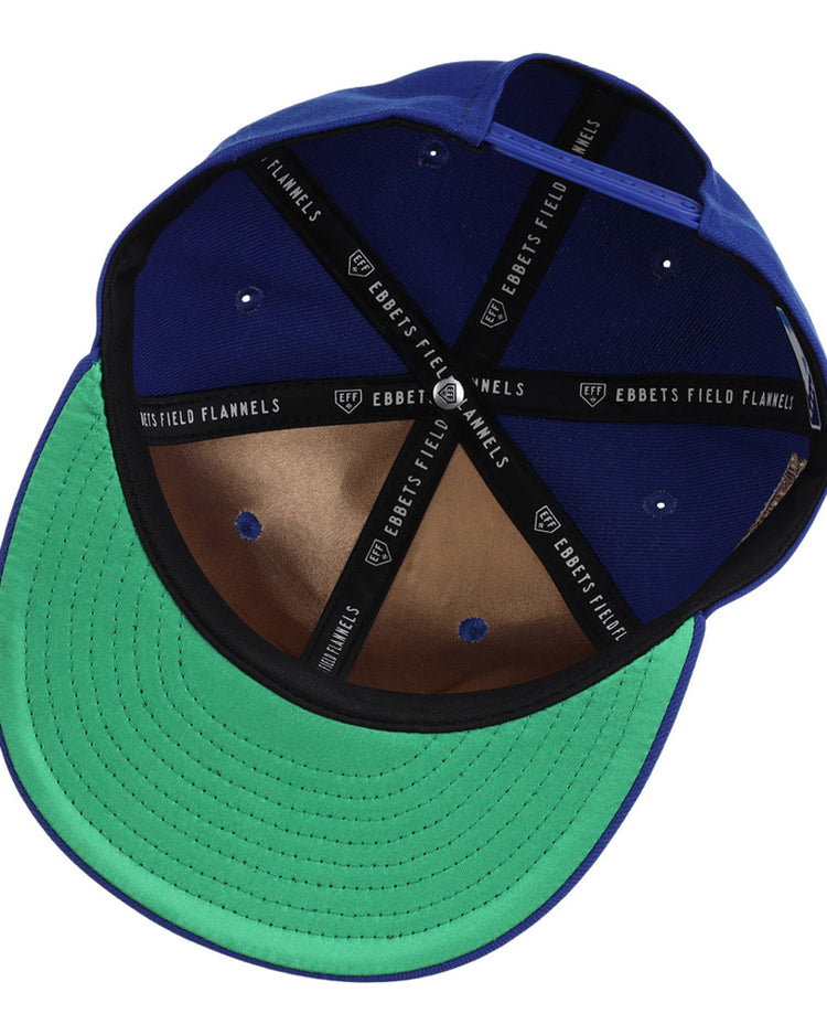 The Ebbets Field Durham Bulls MiLB Snapback Ballcap is shown upside down, revealing its green underside brim, brown leather inner panel, black sweatband, and interior taping labeled EBBETS FIELD FLANNELS.