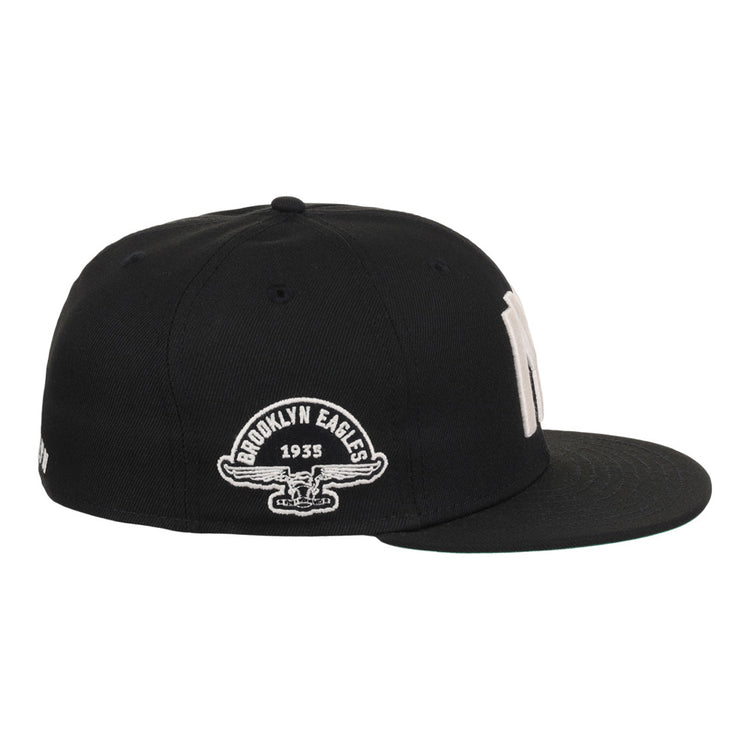 The Ebbets Field Brooklyn Eagles NLB Fitted Ballcap is a black cap with a flat brim, featuring “Brooklyn Eagles 1935” and an eagle graphic embroidered in white on the side.