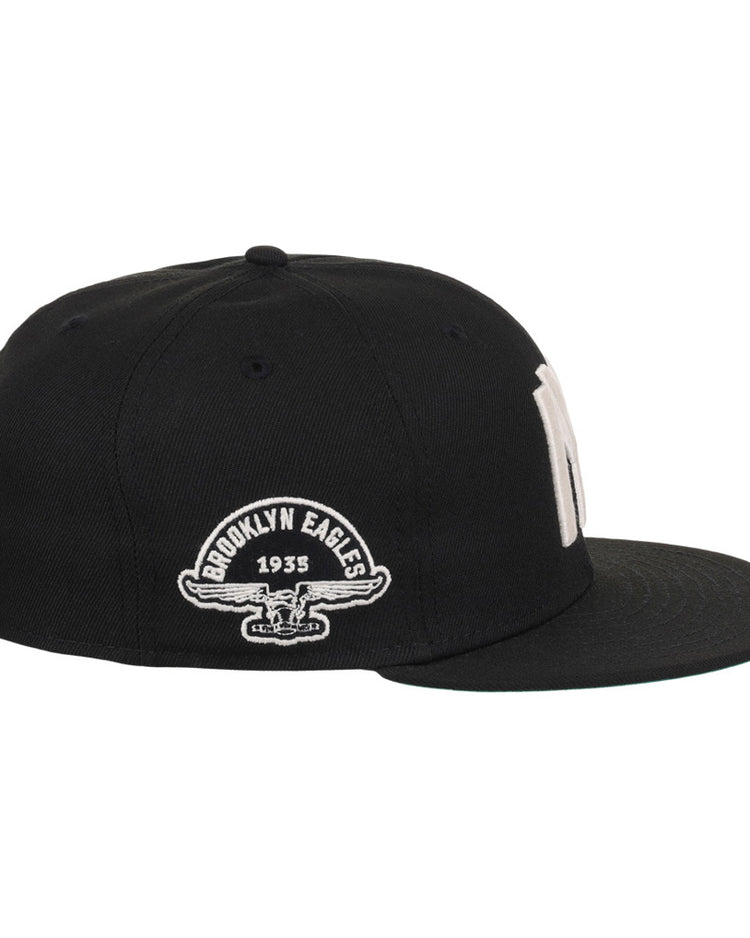 The Ebbets Field Brooklyn Eagles NLB Fitted Ballcap is a black cap with a flat brim, featuring “Brooklyn Eagles 1935” and an eagle graphic embroidered in white on the side.