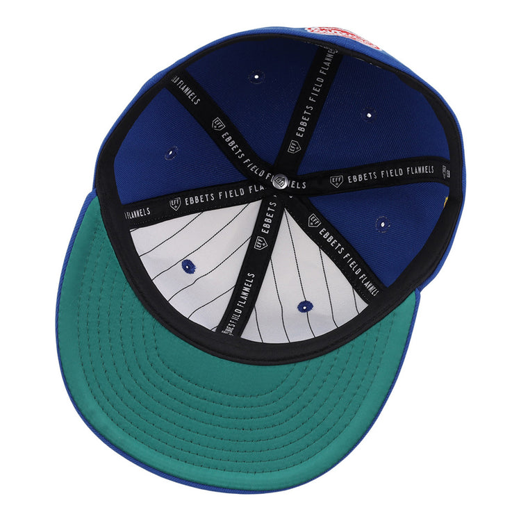 The image shows the inside of the Santurce Cangrejeros Wordmark Chainstitch Fitted Ballcap by Ebbets Field—a blue cap with a green brim, black Ebbets Field bands, and a white pinstriped lining with ventilation eyelets.