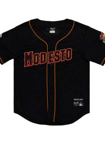 The Ebbets Field Modesto Nuts MiLB Button Down Jersey is a black baseball jersey with orange and red trim, MODESTO in bold red letters on the chest, and team logos on both sleeves.