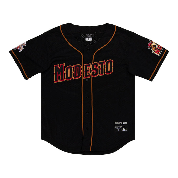 The Ebbets Field Modesto Nuts MiLB Button Down Jersey is a black baseball jersey with orange and red trim, MODESTO in bold red letters on the chest, and team logos on both sleeves.