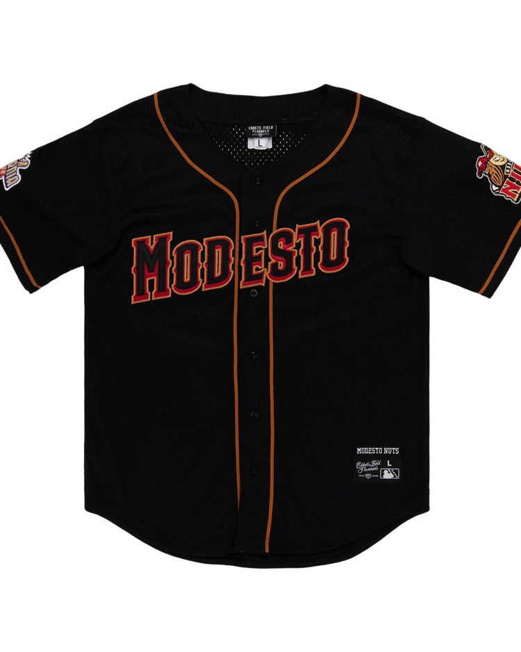 The Ebbets Field Modesto Nuts MiLB Button Down Jersey is a black baseball jersey with orange and red trim, MODESTO in bold red letters on the chest, and team logos on both sleeves.