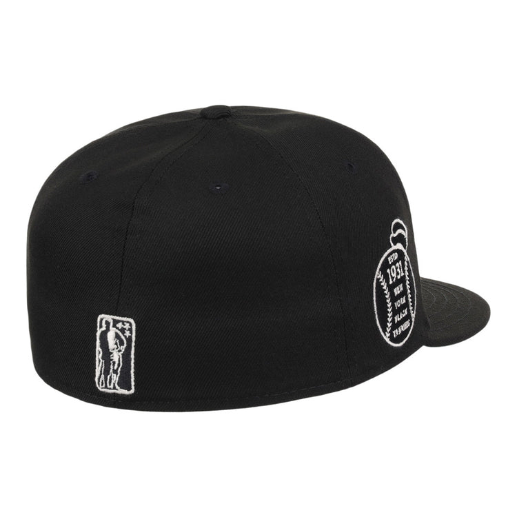The Ebbets Field New York Black Yankees NLB Black/White Fitted Ballcap is shown from the back, with white embroidered patches—a small figure on the left and a football-shaped design with text on the right.