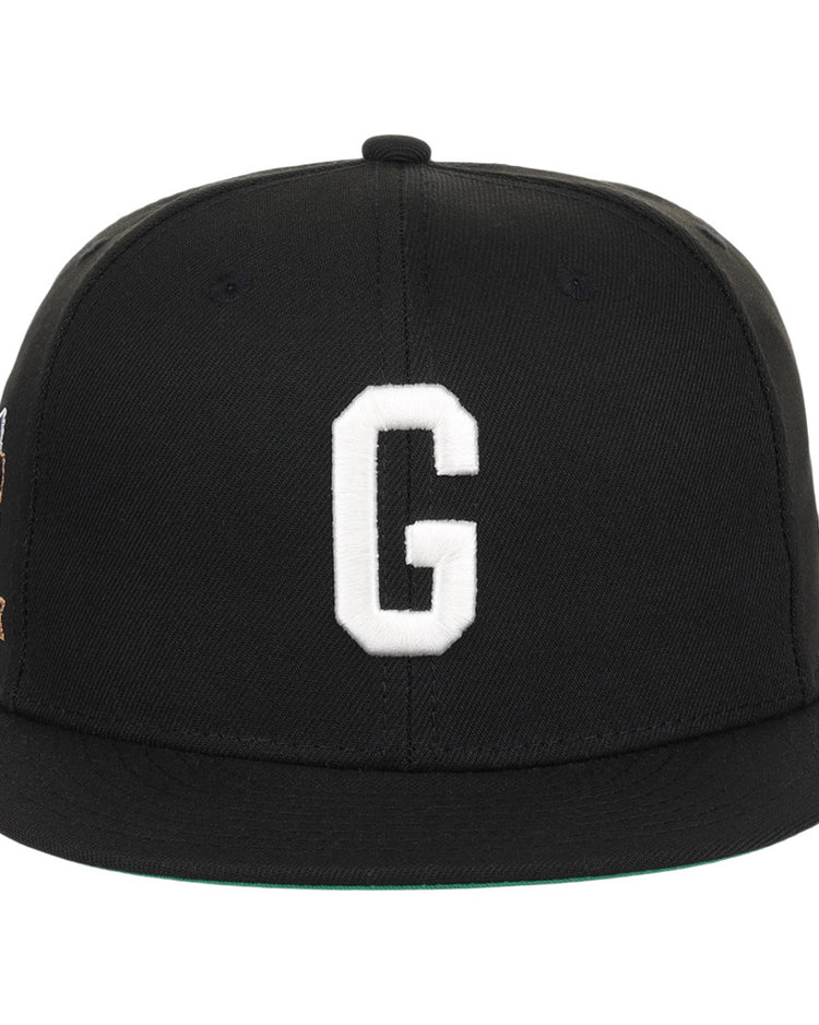 The Ebbets Field Homestead Grays NLB Tc Fitted Ballcap is a black cap with a flat brim, featuring a large white embroidered letter G on the front and minimal visible detailing.