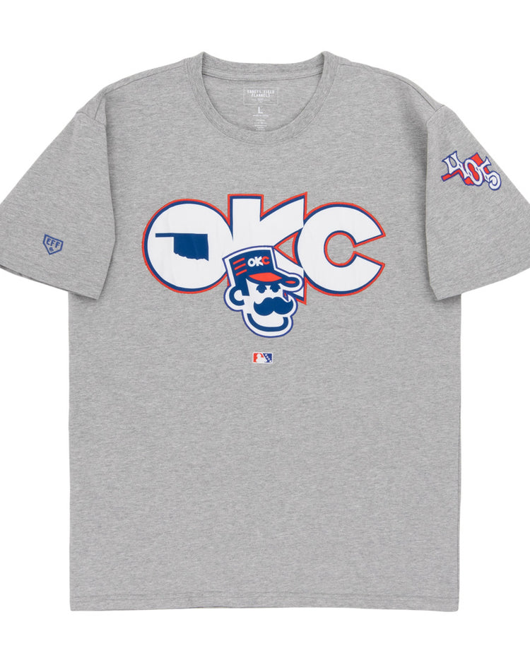 The Ebbets Field Oklahoma City 89Ers MiLB Fashion Cotton Short Sleeve Tee is a heather gray T-shirt with a large logo and cartoon character on the chest, plus 405 patches and other symbols on the sleeves.