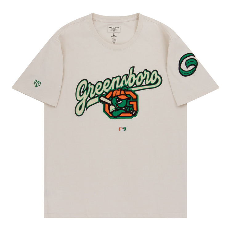 The Ebbets Field Greensboro Grasshoppers MiLB Fashion Cotton Short Sleeve Tee is a beige shirt with a bold Greensboro script, cartoon eye, and orange slices on the chest, plus green logos on the sleeves.