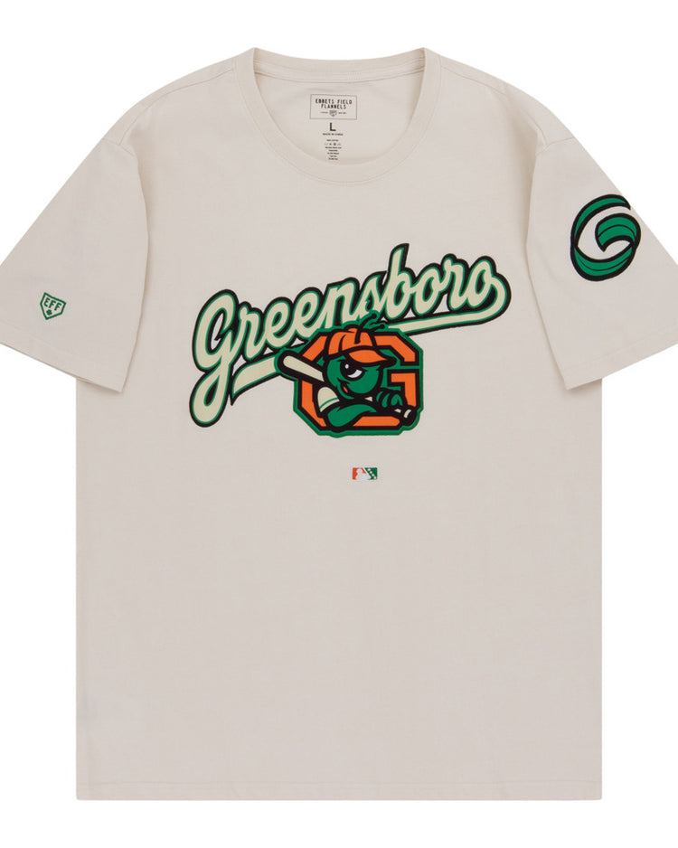 The Ebbets Field Greensboro Grasshoppers MiLB Fashion Cotton Short Sleeve Tee is a beige shirt with a bold Greensboro script, cartoon eye, and orange slices on the chest, plus green logos on the sleeves.