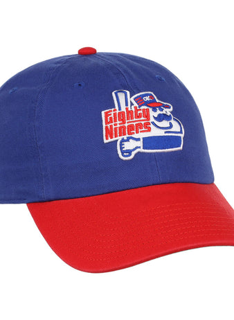 The Ebbets Field Oklahoma City 89Ers MiLB Logo Dad Ballcap is blue with a red brim, featuring an embroidered cartoon character holding a bat and “Eighty Niners” text on the front.