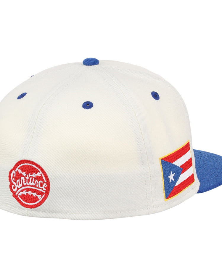 The Ebbets Field Santurce Cangrejeros Chainstitch Fitted Ballcap is white with a blue brim, a red circular Santurce logo, and a Puerto Rican flag patch on the side.