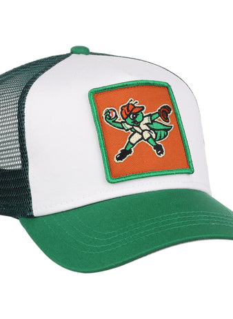 The Greensboro Grasshoppers MiLB Trucker Ballcap by Ebbets Field is a green and white mesh-back hat featuring a front patch with a cartoon leprechaun mascot in a fighting stance on an orange background.