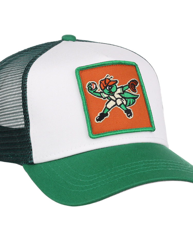 The Greensboro Grasshoppers MiLB Trucker Ballcap by Ebbets Field is a green and white mesh-back hat featuring a front patch with a cartoon leprechaun mascot in a fighting stance on an orange background.
