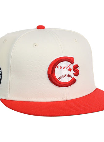 The Vancouver Canadians MiLB Snapback Ballcap by Ebbets Field is a cream cap with a red brim, featuring a red and white C logo with baseball stitching on the front and a circular patch with trees and text on the side.