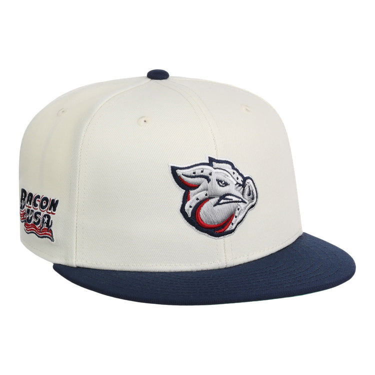 The Lehigh Valley Ironpigs MiLB Snapback Ballcap by Ebbets Field features a cream crown, navy brim, stylized pig logo on the front, and Bacon USA text with an American flag graphic on the side.