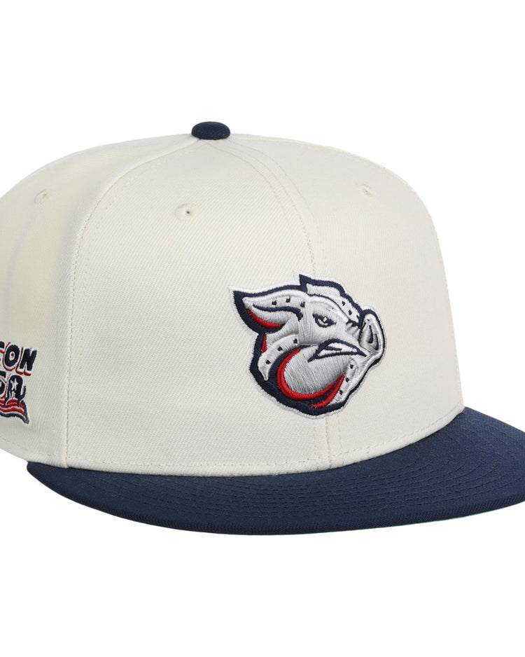 The Lehigh Valley Ironpigs MiLB Snapback Ballcap by Ebbets Field features a cream crown, navy brim, stylized pig logo on the front, and Bacon USA text with an American flag graphic on the side.