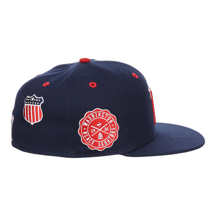 The Ebbets Field Washington Black Senators NLB Varsity Fitted Ballcap is a navy blue cap with a flat brim, detailed with red and white embroidered shield and circular Washington Senators logo patches on the side.