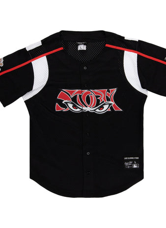 The Ebbets Field Lake Elsinore Storm MiLB Button Down Jersey is a black short-sleeve baseball jersey with white and red accents, mesh panels, a stylized eyes logo on the chest, and patches on the left sleeve and lower right front.
