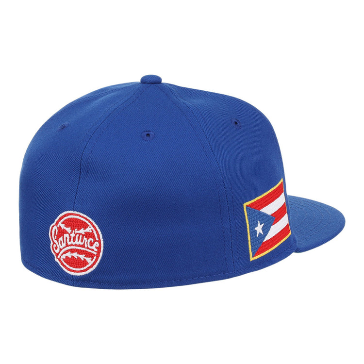 The Santurce Cangrejeros Wordmark Chainstitch Fitted Ballcap by Ebbets Field is a blue cap with a red circular Santurce logo on the back and a Puerto Rican flag patch on the side.