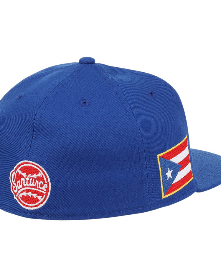 The Santurce Cangrejeros Wordmark Chainstitch Fitted Ballcap by Ebbets Field is a blue cap with a red circular Santurce logo on the back and a Puerto Rican flag patch on the side.