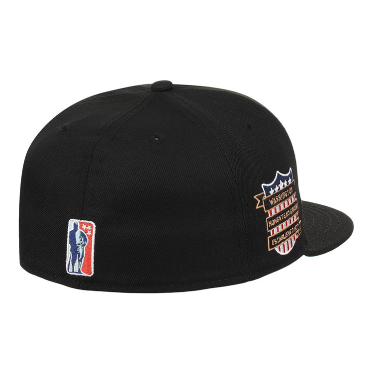 The Ebbets Field Homestead Grays NLB Tc Fitted Ballcap is a black cap featuring a small blue and white basketball player silhouette embroidered on the back and a multicolored shield patch with text on the side.