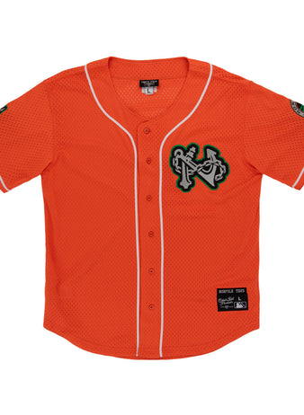 The Ebbets Field Norfolk Tides MiLB Button Down Jersey features orange fabric with white trim, a green-and-white chest logo patch, sleeve patches, a button front, and a black manufacturer's label above the hem.