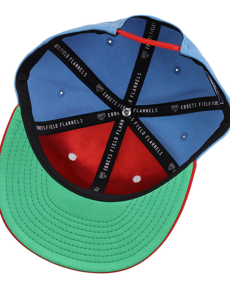 An upside-down Ebbets Field Corpus Christi Hooks MiLB Snapback Ballcap shows a blue crown, red inner front panel, green brim underside, black sweatband, and black EBBETS FIELD FLANNELS branded taping.