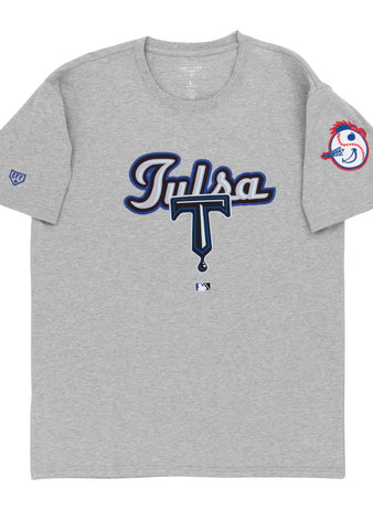 The Ebbets Field Tulsa Drillers MiLB Fashion Cotton Short Sleeve Tee is a gray shirt with “Tulsa” in blue and white script and a large T on the front. The left sleeve features the Drillers’ baseball mascot head with a red feather headband.