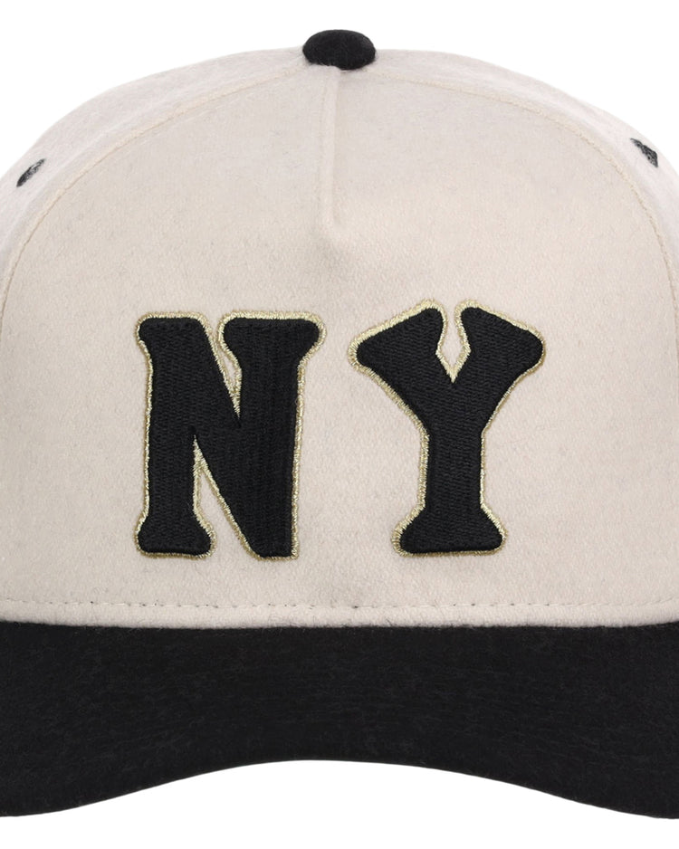 The Ebbets Field New York Black Yankees NLB Ballpark A-Frame Ballcap is beige with a black brim and features large black “NY” letters outlined in gold on the front.