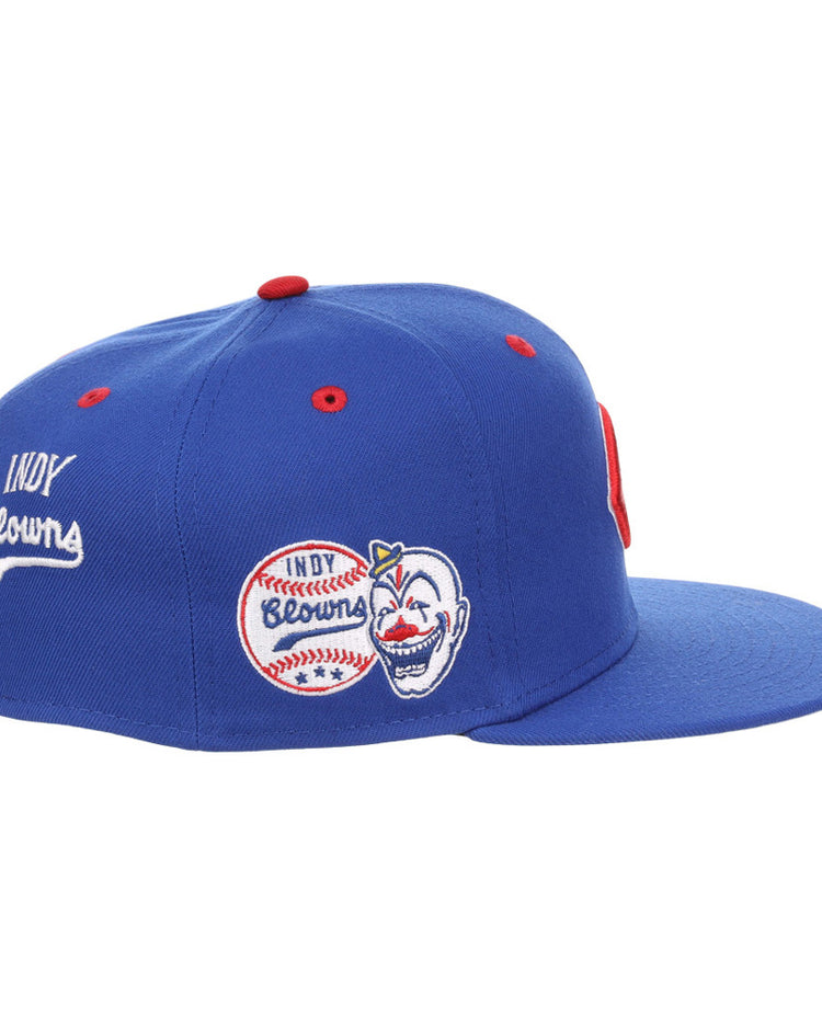 The Ebbets Field Indianapolis Clowns NLB Varsity Fitted Ballcap is a blue cap with a red top button, embroidered Indy Browns baseball graphics, a smiling clown face on the side, and white 