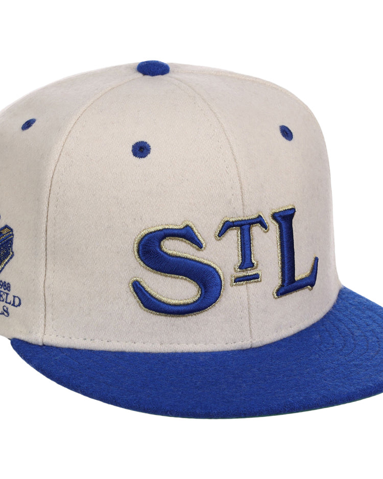 The Ebbets Field St. Louis Stars NLB Ballpark Fitted Ballcap features a white crown, blue brim and button, “STL” embroidered on the front, and a “Shea’s Field 1988 Panels” patch on the side.