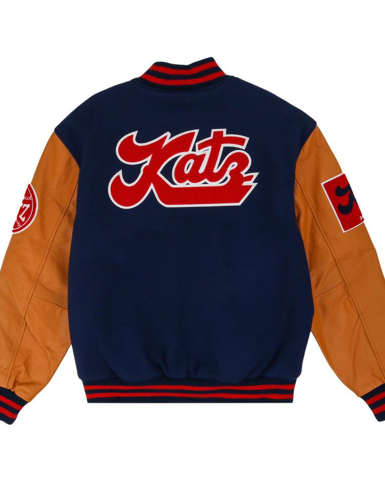 The Ebbets Field Kansas City Katz Dna Varsity Jacket has a navy body, tan sleeves, red accents, a large red and white Katz patch on the back, and round plus square patches on the sleeves.