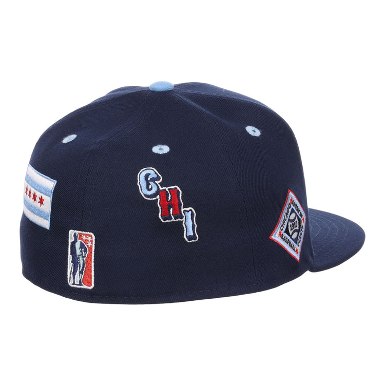 The Ebbets Field Chicago American Giants NLB Varsity Fitted Ballcap is a navy blue cap with embroidered patches—a Chicago flag, CHI letters, baseball player silhouette, and diamond-shaped logo—on the back and side.