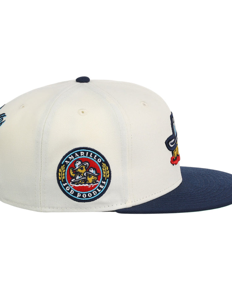 The Ebbets Field Amarillo Sod Poodles MiLB Snapback Ballcap is white and navy with a round team logo patch on the side, a blue brim, and colorful embroidered designs on the front.