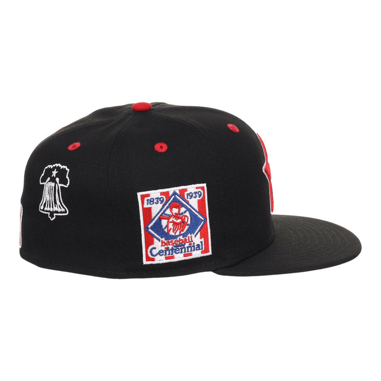 The Ebbets Field Philadelphia Stars NLB Varsity Fitted Ballcap is a black cap with red accents, flat brim, vent holes, and side embroidered patches—a Baseball Centennial 1839-1939 logo and a white outlined bell.