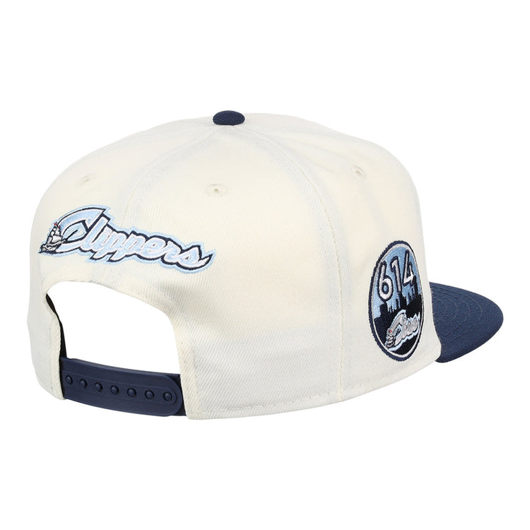 The Ebbets Field Columbus Clippers MiLB Snapback Ballcap features a cream crown, navy brim, script Clippers embroidery on the back, and a side patch with 613 and a city skyline.