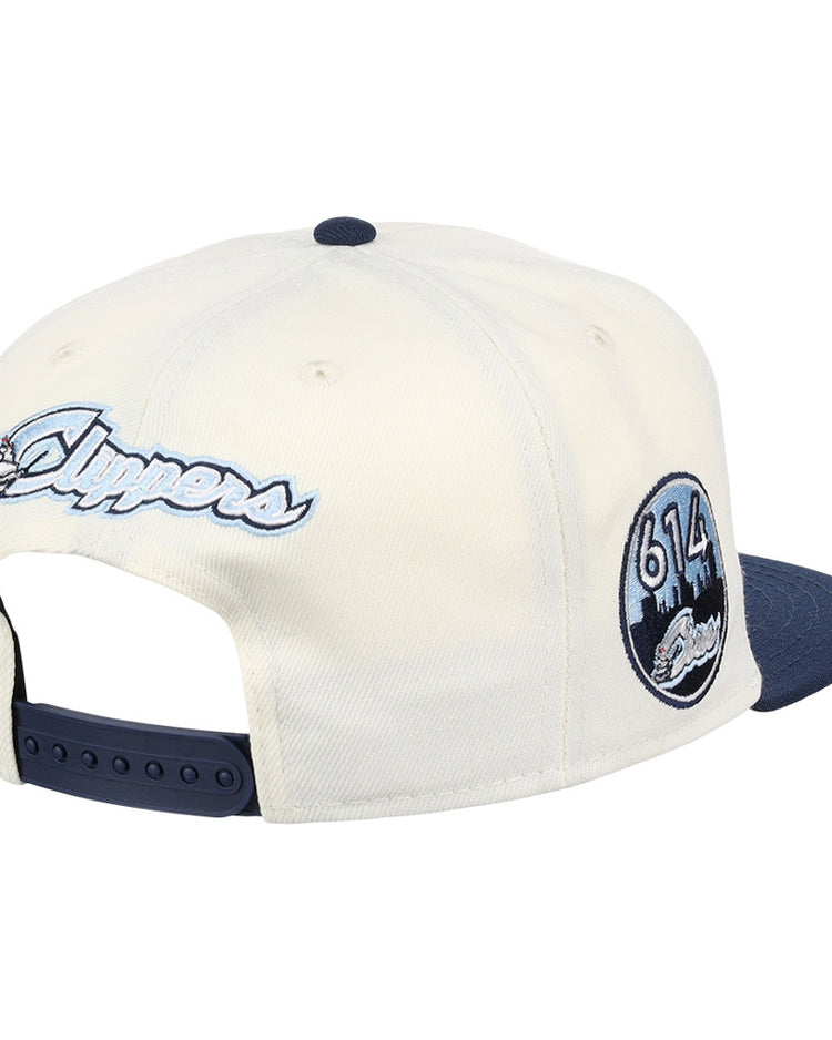 The Ebbets Field Columbus Clippers MiLB Snapback Ballcap features a cream crown, navy brim, script Clippers embroidery on the back, and a side patch with 613 and a city skyline.